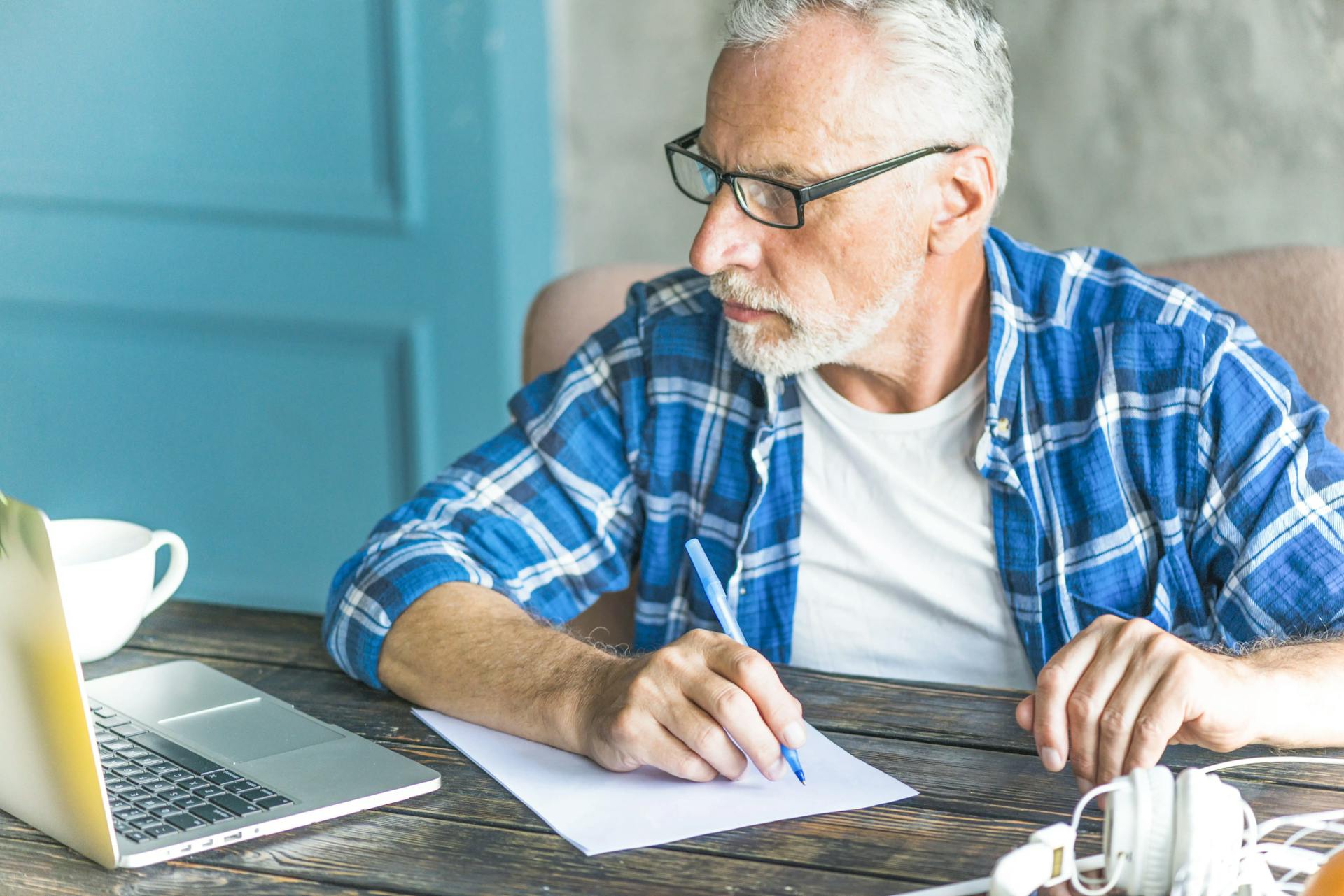 homem idoso lendo notícia no notebook e fazendo anotação no caderno